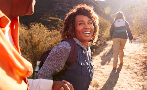 A smiling woman helping an older man on a trail in the countryside.